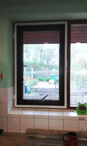 A white screen and sub frame on a brown framed window in a commercial kitchen