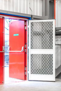 Half of a double action fly screen double door on a red fire exit door in a warehouse