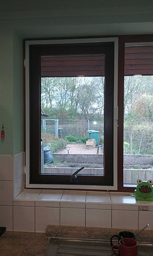 A white fly screen window installed on a brown framed window in a commercial kitchen