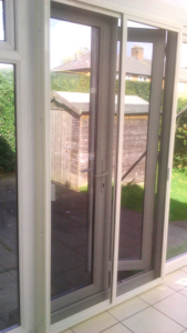 White sliding patio screen door installed on a conservatory door with shed in the background in the garden