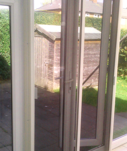 White sliding patio screen door installed on a conservatory door with shed in the background in the garden