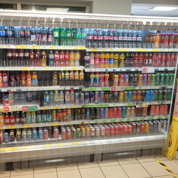 A supermarket aisle filled with bottles and canned drinks behind pvc strips