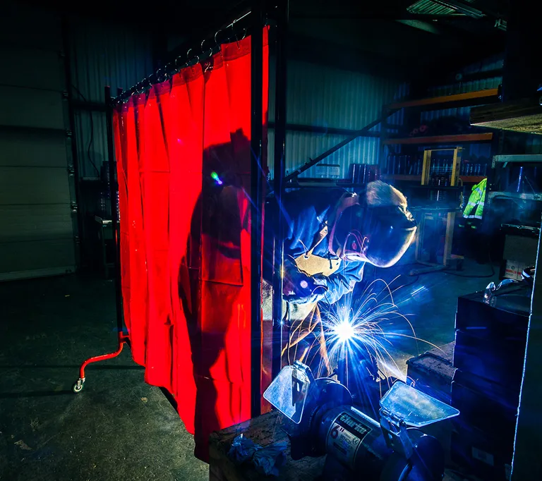 Worker welding behind a red welding screen